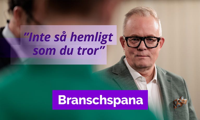 En man i kostym och glasögon som pratar med en annan man.