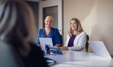 Två kvinnor som sitter vid ett bord med en bärbar dator.