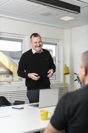 Foto av leende Marko Vikman stående vid dator och skrivbord.