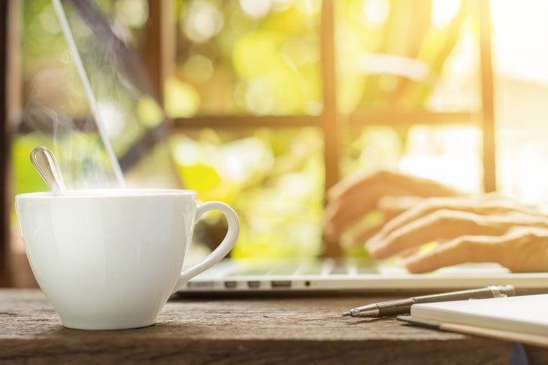 vit kaffekopp med person i bakgrunden som arbetar pa laptop